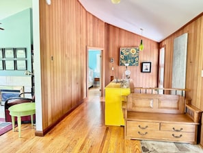 Quarto com paredes de madeira, uma ilha de cozinha amarela, um banco de madeira e uma cadeira verde.