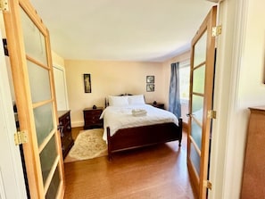 Quarto com cama de madeira, mesa de cabeceira, cômoda e porta com painéis de vidro jateado.