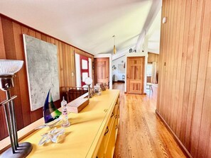 Un couloir aux murs recouverts de lambris en bois, un comptoir jaune sur lequel sont disposés divers objets, et une porte qui mène à une autre pièce.
