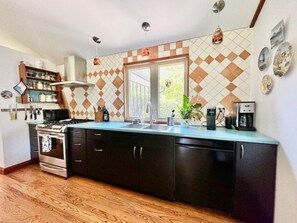 A kitchen with a central island, a stove, a sink, and a coffee maker. - Porchside Retreat: Sauna and Treeline Backyard (Meaford)
