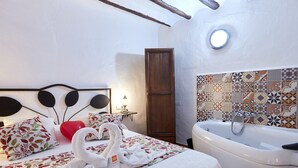 A hotel room with a bed, a red heart-shaped pillow, a white towel, a bathtub, and a patterned tile wall. - Apartment 'Cazorla Rural Guadiana' with Balcony, Wi-Fi and Air Conditioning (QUESADA)