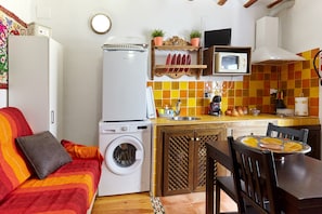 A compact kitchen with a washing machine, a microwave, and a dining area with a table and chairs. - Apartment 'Cazorla Rural Guadiana' with Balcony, Wi-Fi and Air Conditioning (QUESADA)
