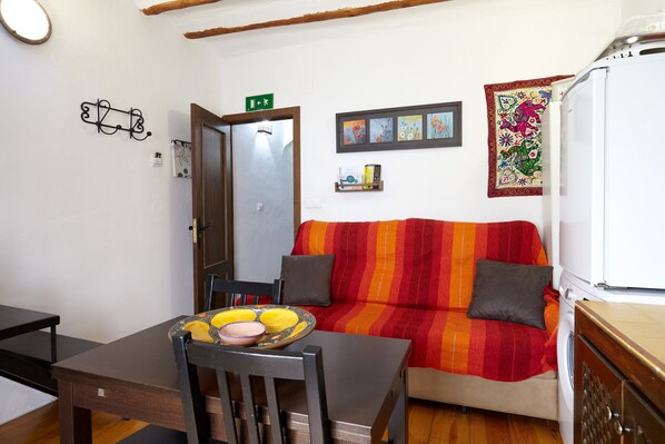 A compact living space with a dining table, a sofa, a washing machine, and a small shelf with items.