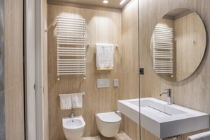 Un baño moderno con un espejo grande, un bidé, un inodoro y un lavamanos.