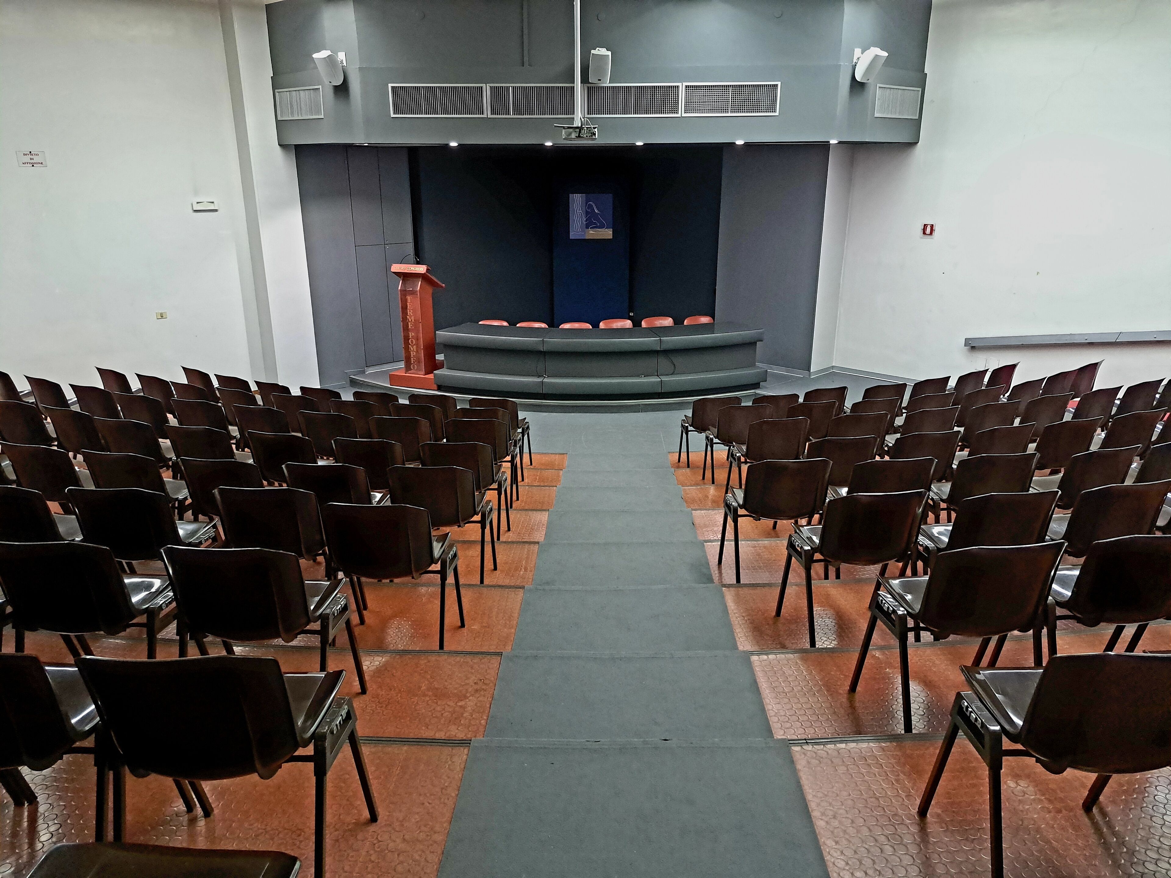 An auditorium with rows of chairs facing a stage with a podium.