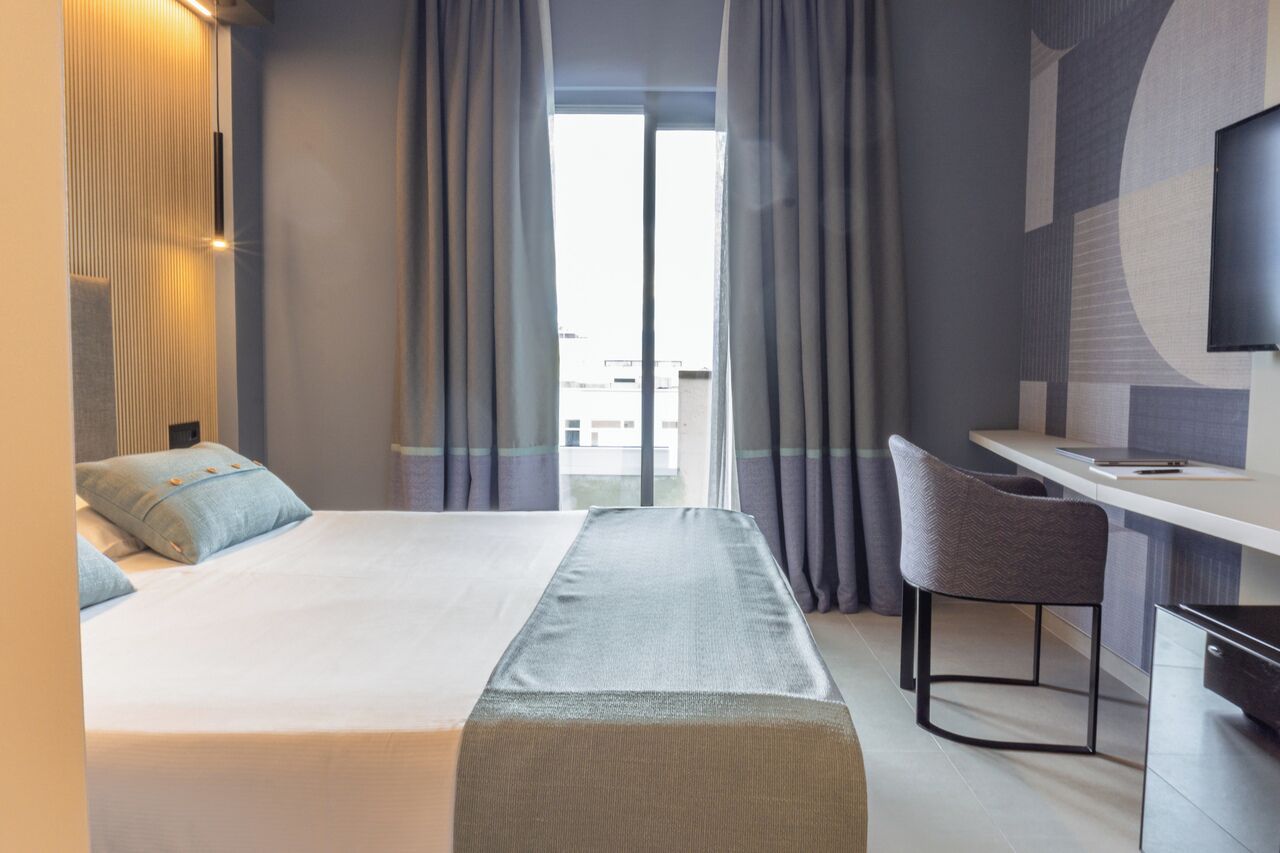 A hotel room with a bed, a desk, a chair, and a TV.