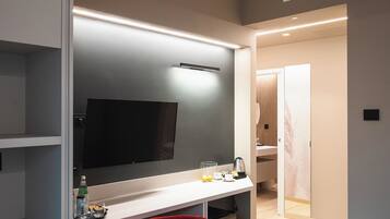 A modern hotel room with a large flat-screen TV, a desk with a tray of breakfast items, and a red chair.