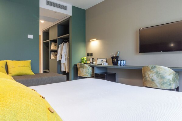 A hotel room with a bed, a desk, a chair, a TV, and a wardrobe.