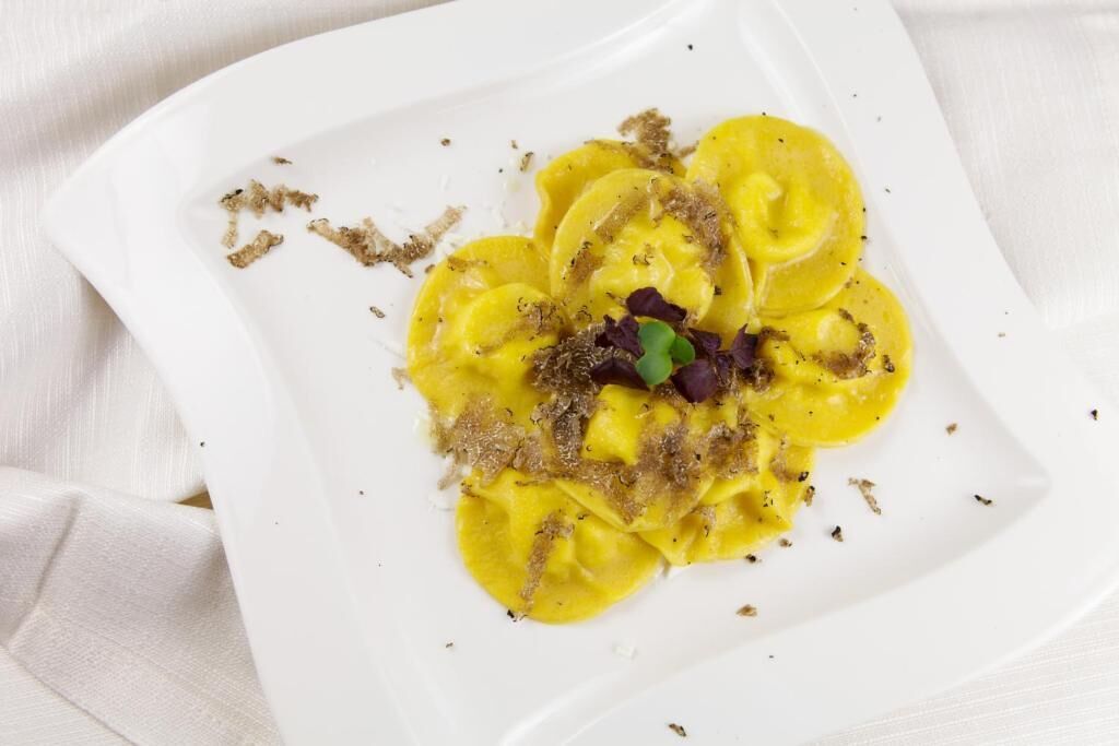 Un plato blanco con ravioles, adornado con hierbas y una hoja verde pequeña.
