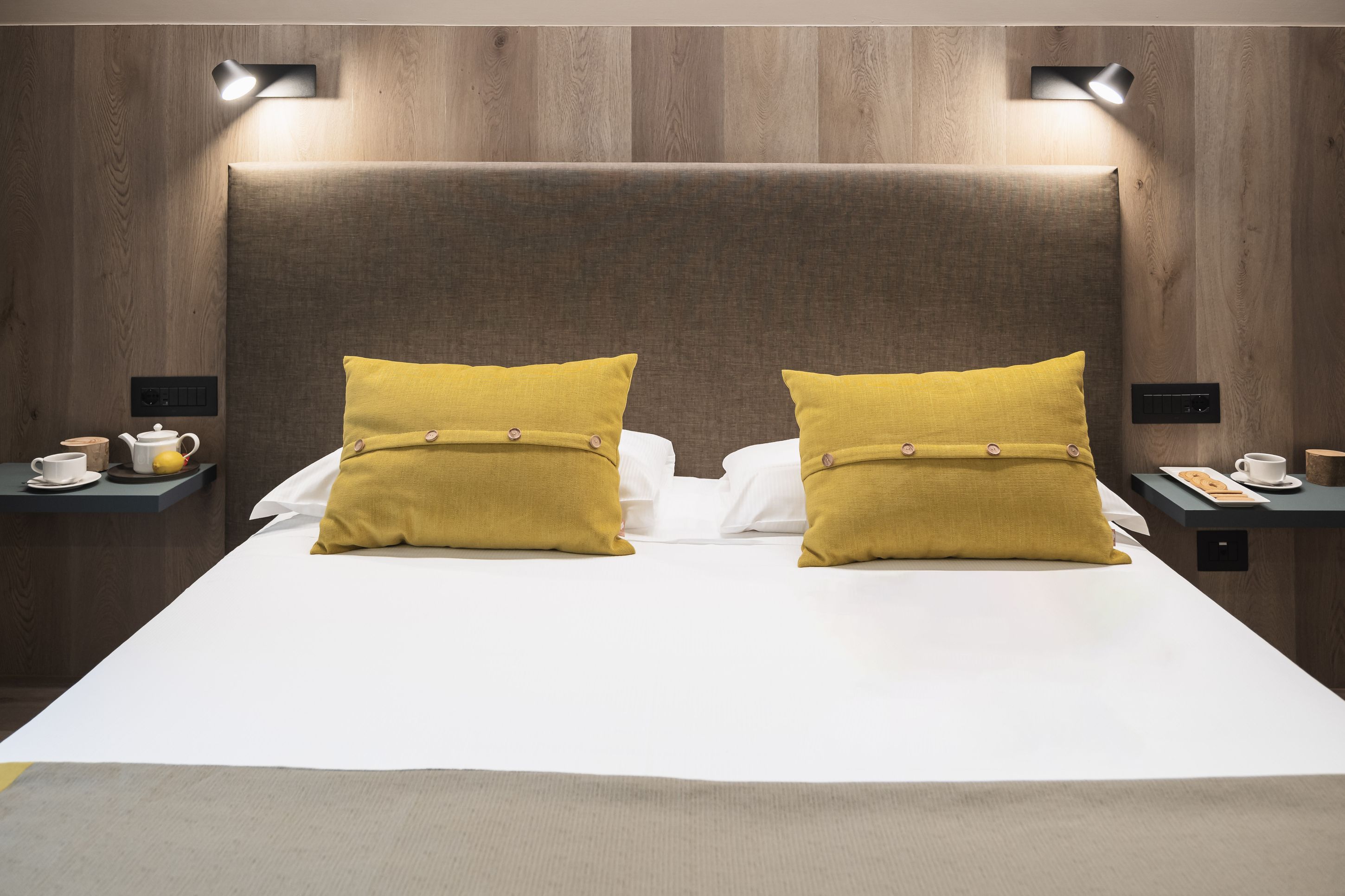 Una habitación de hotel con una cama grande, dos mesitas de noche y un cabecero con iluminación integrada.