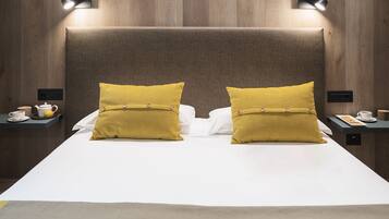 Una habitación de hotel con una cama grande, dos mesitas de noche y un cabecero con iluminación integrada.