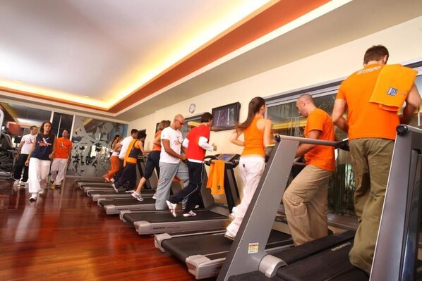 Un gimnasio con cintas de correr alineadas, personas haciendo ejercicio y un reloj en la pared.