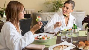 Zwei Personen essen an einem Tisch mit Salat, Wasser und Brot.