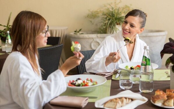 Zwei Personen essen an einem Tisch mit Salat, Wasser und Brot.