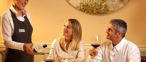 Una mesa de comedor con un camarero sirviendo vino a los comensales.