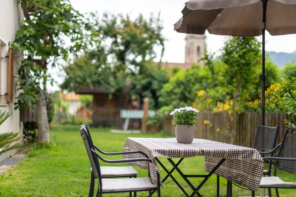 An outdoor patio with a table and chairs, a potted plant, and a view of a building with a bell tower.