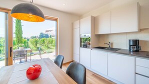 A modern kitchen with white cabinets, a black coffee maker, and a dining area with a table and chairs.