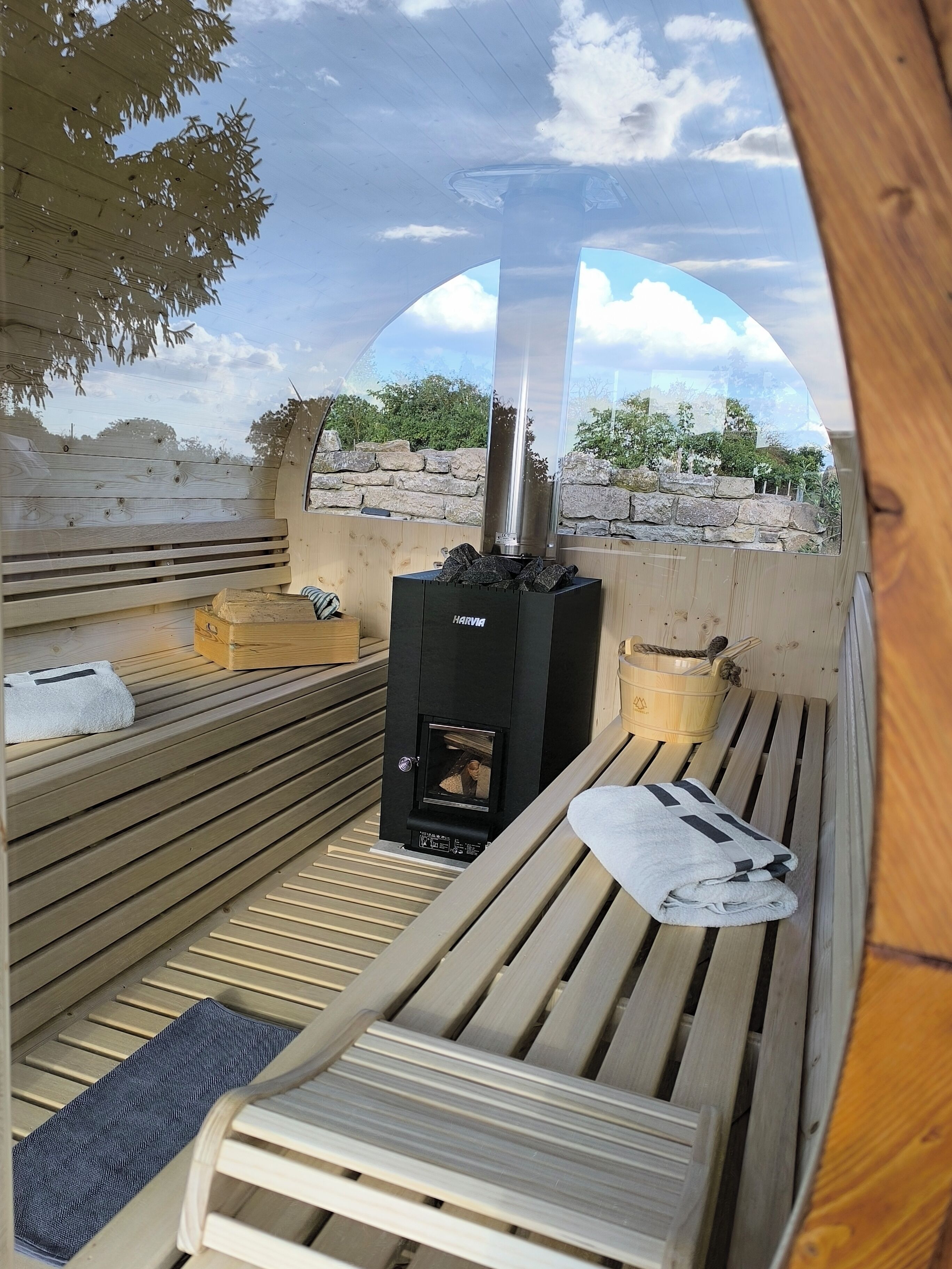 Eine Sauna mit Wand aus Stein, einem Harvia Holzofen und Holzbänken.