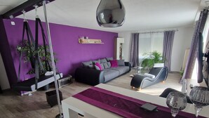 Uma sala de estar moderna com um sofá, uma cadeira balanço, uma mesa de jantar e uma janela grande com cortinas.