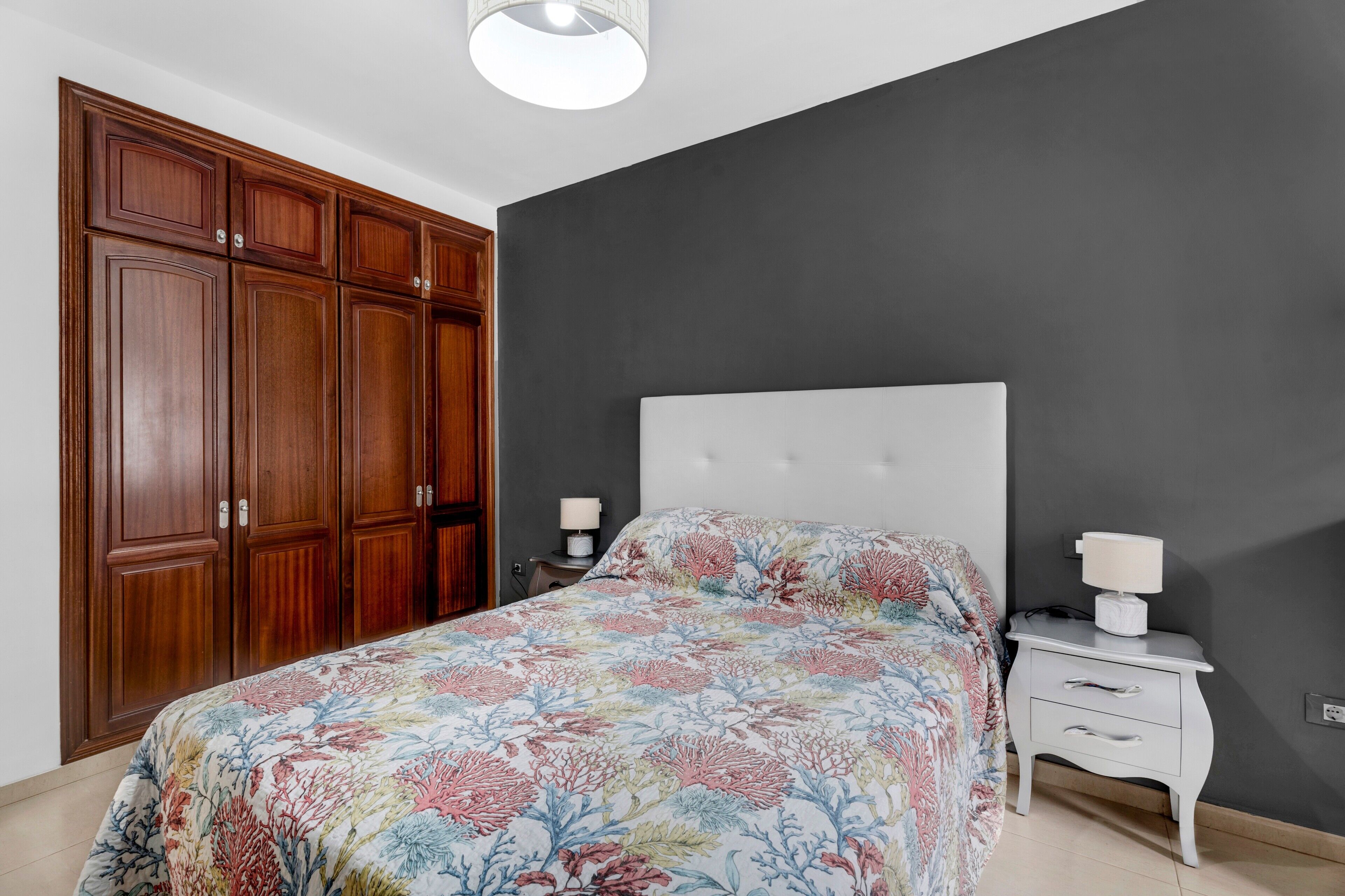 A bedroom with a bed, nightstands, a dresser, and a ceiling light.