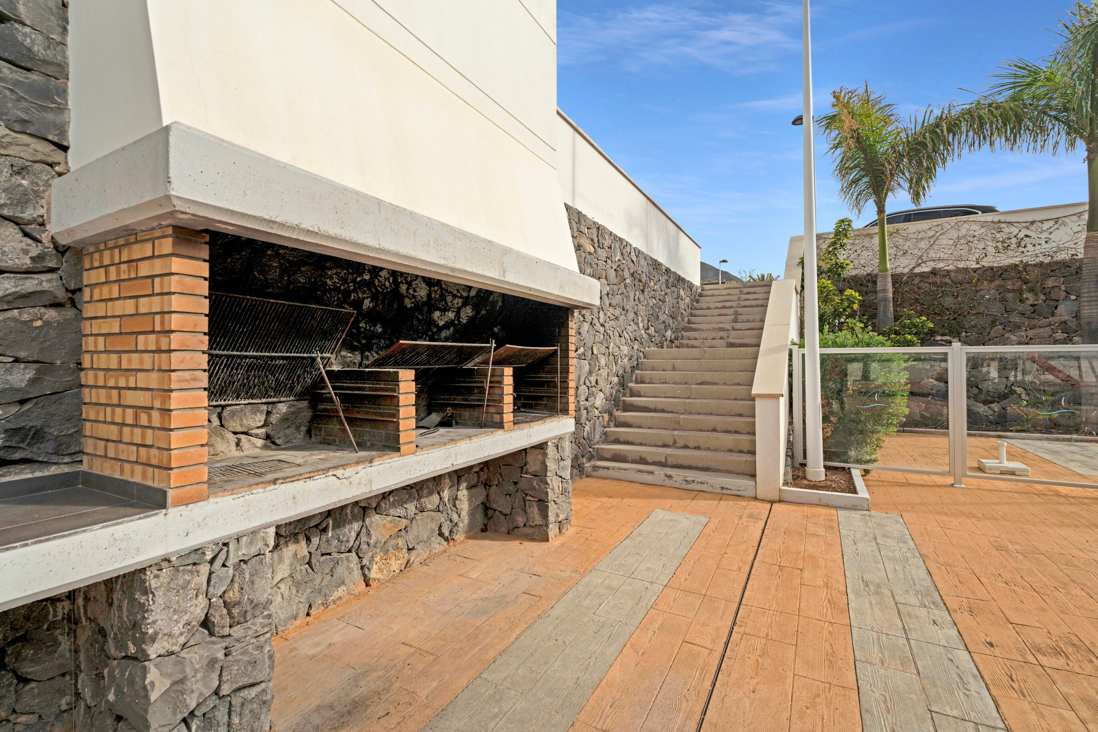 Un espace barbecue extérieur moderne, avec des murs en pierre et une terrasse en bois.