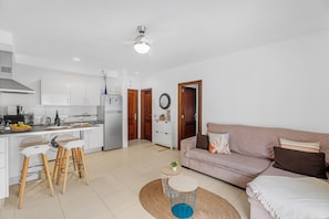 A modern kitchen with white cabinets, a dining area with stools, a round coffee table, and a living area with a sofa and cushions. - Vacation Apartment 'Bajamar En Armonía' with Mountain Views and Wi-Fi (Bajamar)