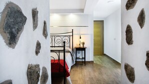 Un dormitorio con una cama, una mesita de noche con lámpara, y una puerta que da a otra habitación.