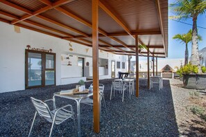 Un espace extérieur aménagé en terrasse, avec des chaises et des tables en métal, un coin salon abrité et une entrée de l’immeuble portant l’inscription « APPARTEMENT ».