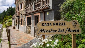 A rustic stone building with a balcony, a wooden sign indicating 'CASA RURAL Mirador del Navia,' and a paved pathway. - Holiday Home 'Mirador Del Navia' with Mountain View, Private Terrace and Wi-Fi (Serandinas)