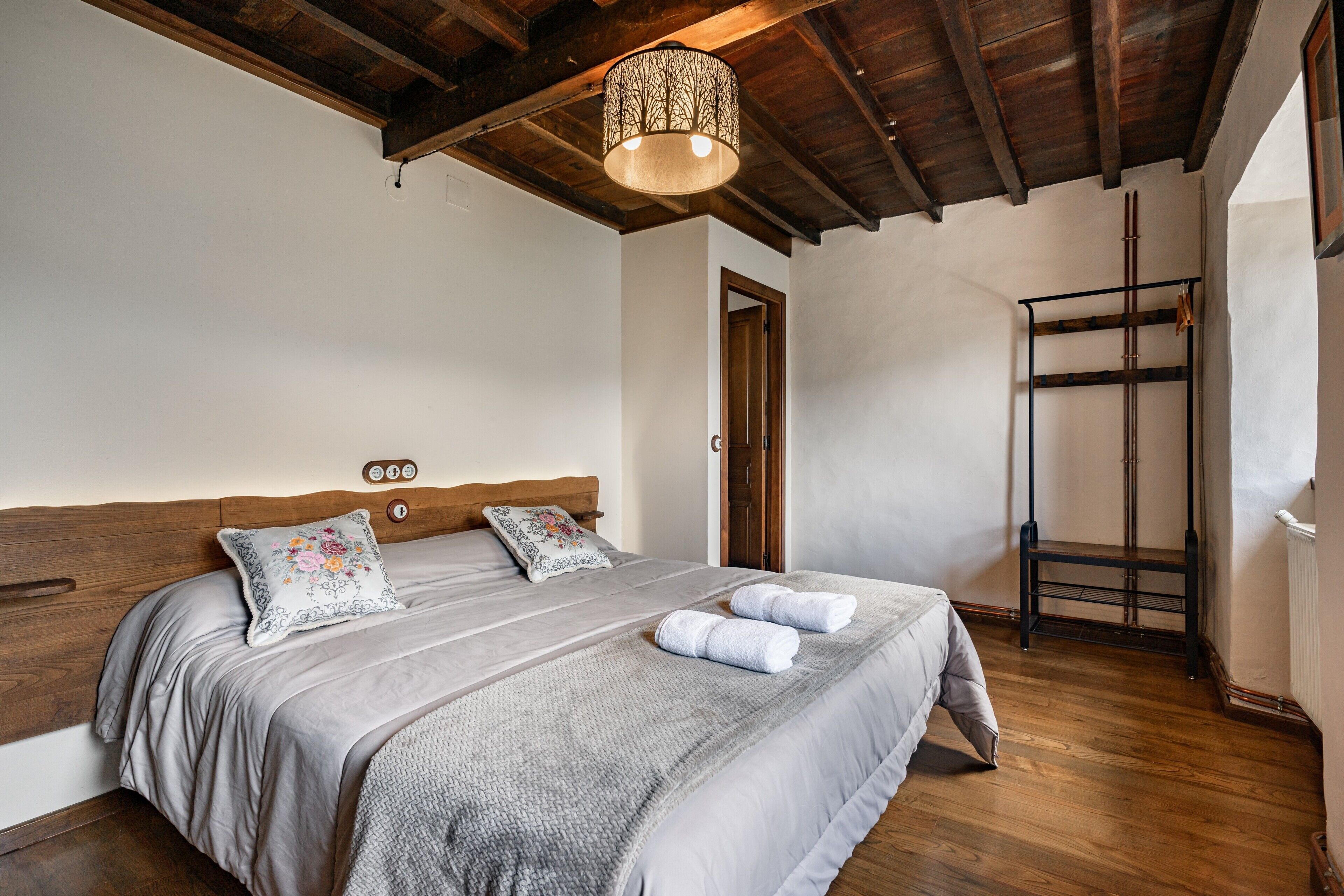 Een slaapkamer met een houten hoofdbord, een bed met grijze beddengoed, een hanglamp en een houten ladder tegen de muur.