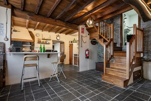 A kitchen with a bar area, wooden staircase, stone walls, and a fire extinguisher.