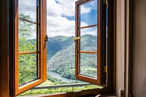 An open window with a view of a mountainous landscape and a river.