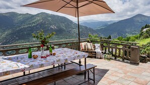 A terrace with a table set for dining, a bench, and a large umbrella. - Holiday Home 'Mirador Del Navia' with Mountain View, Private Terrace and Wi-Fi (Serandinas)