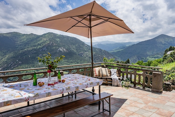 A terrace with a table set for dining, a bench, and a large umbrella.
