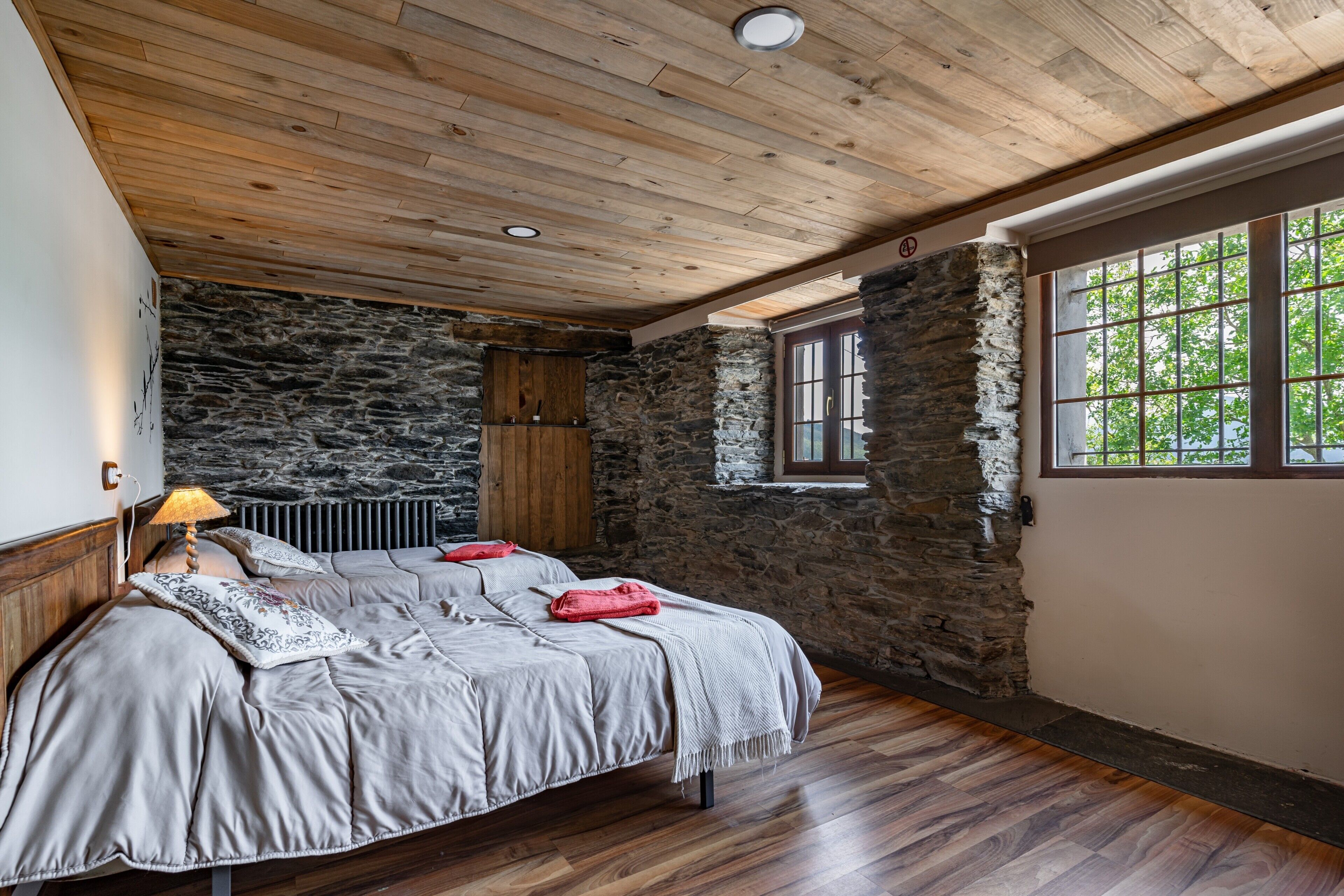 Un dormitorio con pared de piedra, techo de madera y un ventanal grande.