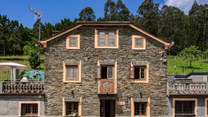 A stone building with multiple windows, a balcony, and a fenced courtyard. - Holiday Home 'Mirador Del Navia' with Mountain View, Private Terrace and Wi-Fi (Serandinas)