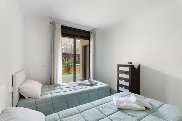 Ein Schlafzimmer mit zwei Betten, einem Schminktisch und einer Glasschiebetür, die auf einen Balkon führt.