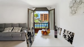 A living room with a grey sofa, a dining table with chairs, a fruit bowl, and a bottle of wine. - Vacation Apartment 'Apto El Mocan Swimming Pool 2bed' with Shared Pool, Private Terrace and Wi-Fi (Palm-Mar)