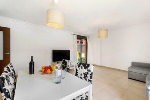 Uma sala de estar moderna com sofá, mesa de jantar com cadeiras, televisão e janela com cortinas.