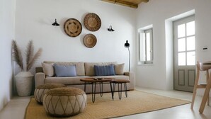 A living room with a sofa, coffee table, and decorative plates on the wall. - Holiday Home 'Agapi Home' with Private Terrace, Wi-Fi and Air Conditioning (Tinos)