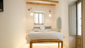 A bedroom with a bed, bench, bedside lamps, and a window. - Holiday Home 'Agapi Home' with Private Terrace, Wi-Fi and Air Conditioning (Tinos)