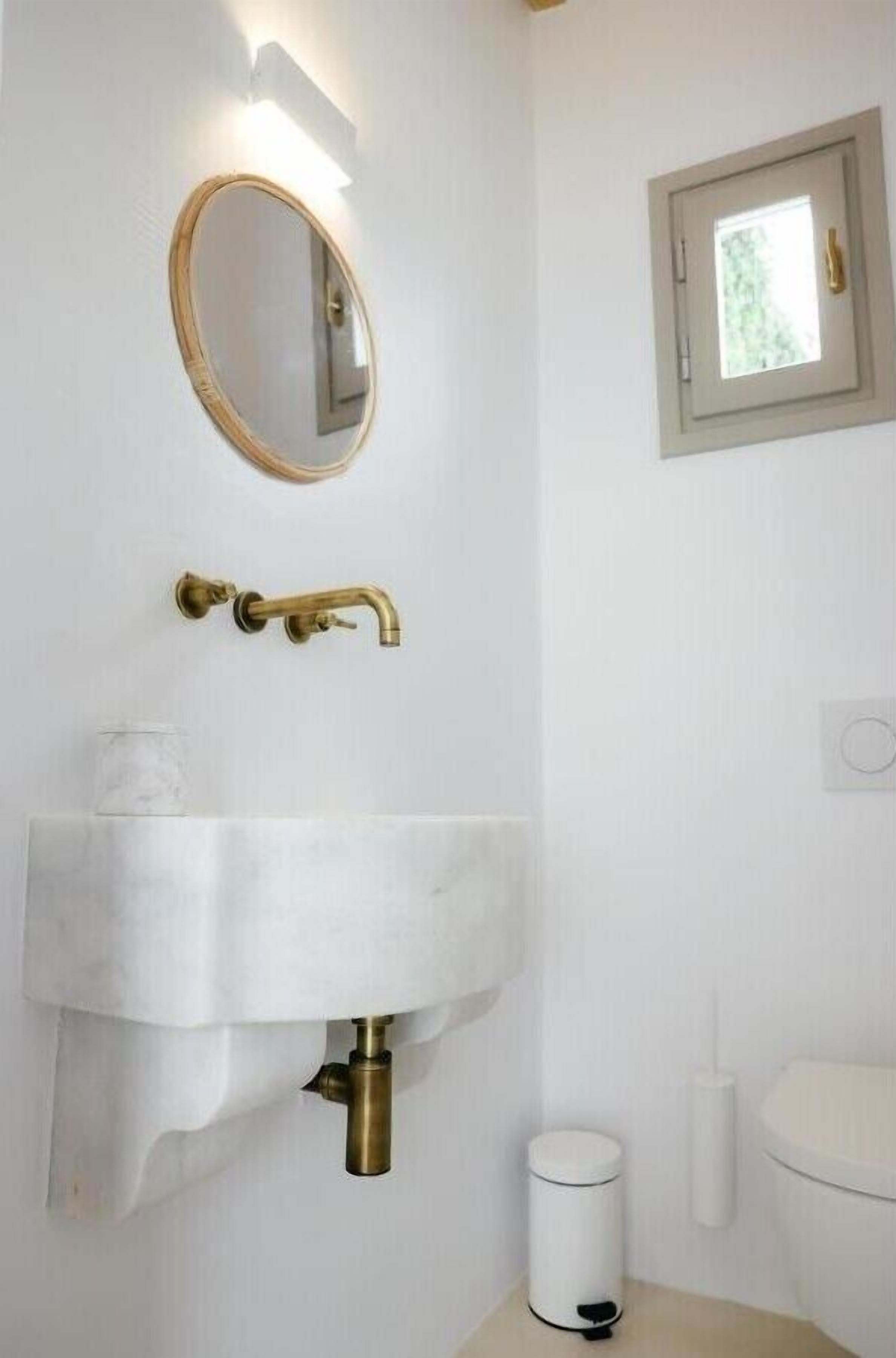A bathroom with a white sink, brass faucet, and a round mirror.