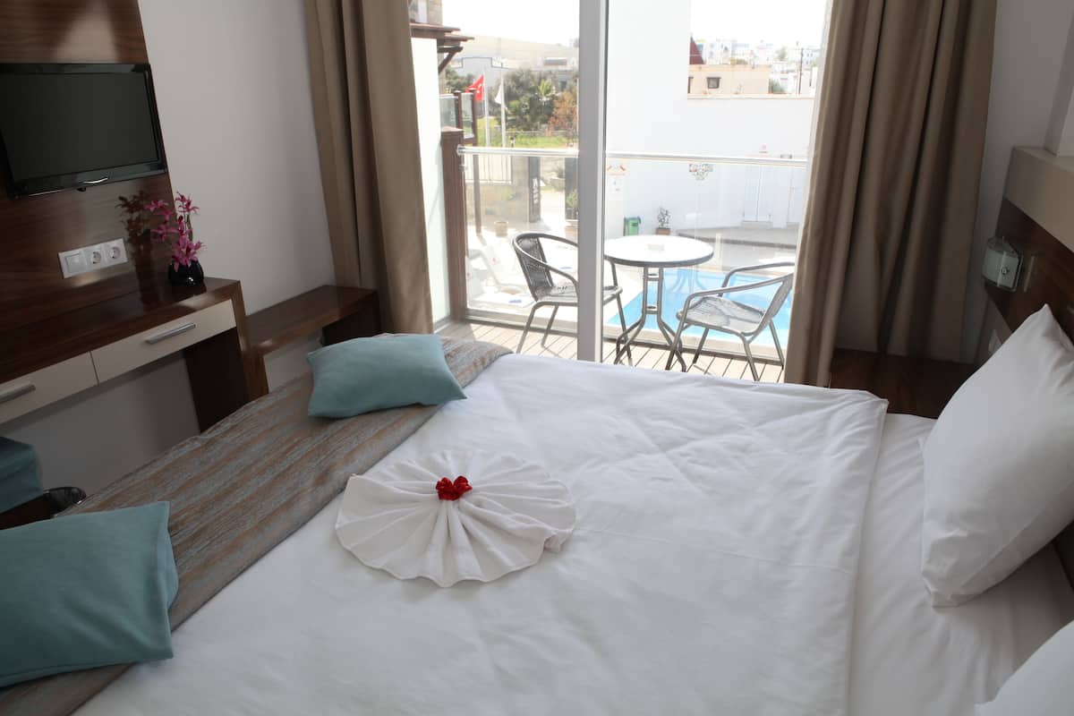 Habitación de hotel con cama, televisor, escritorio, silla y balcón con piscina.