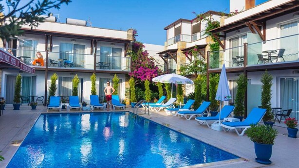 A swimming pool with lounge chairs and umbrellas, surrounded by buildings with balconies and outdoor seating. - Cotton Boutique Hotel (Bodrum)