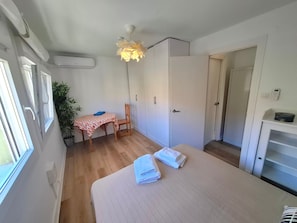 Una stanza con un letto, un tavolo con una sedia, una pianta in vaso e un armadio.