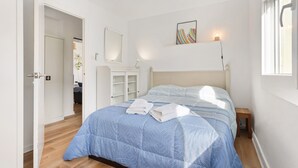 A bedroom with a bed, a bedside table, a nightstand, a mirror, and a shelf with a picture.