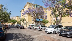 A parking lot with cars, a building with balconies, and trees with purple flowers.