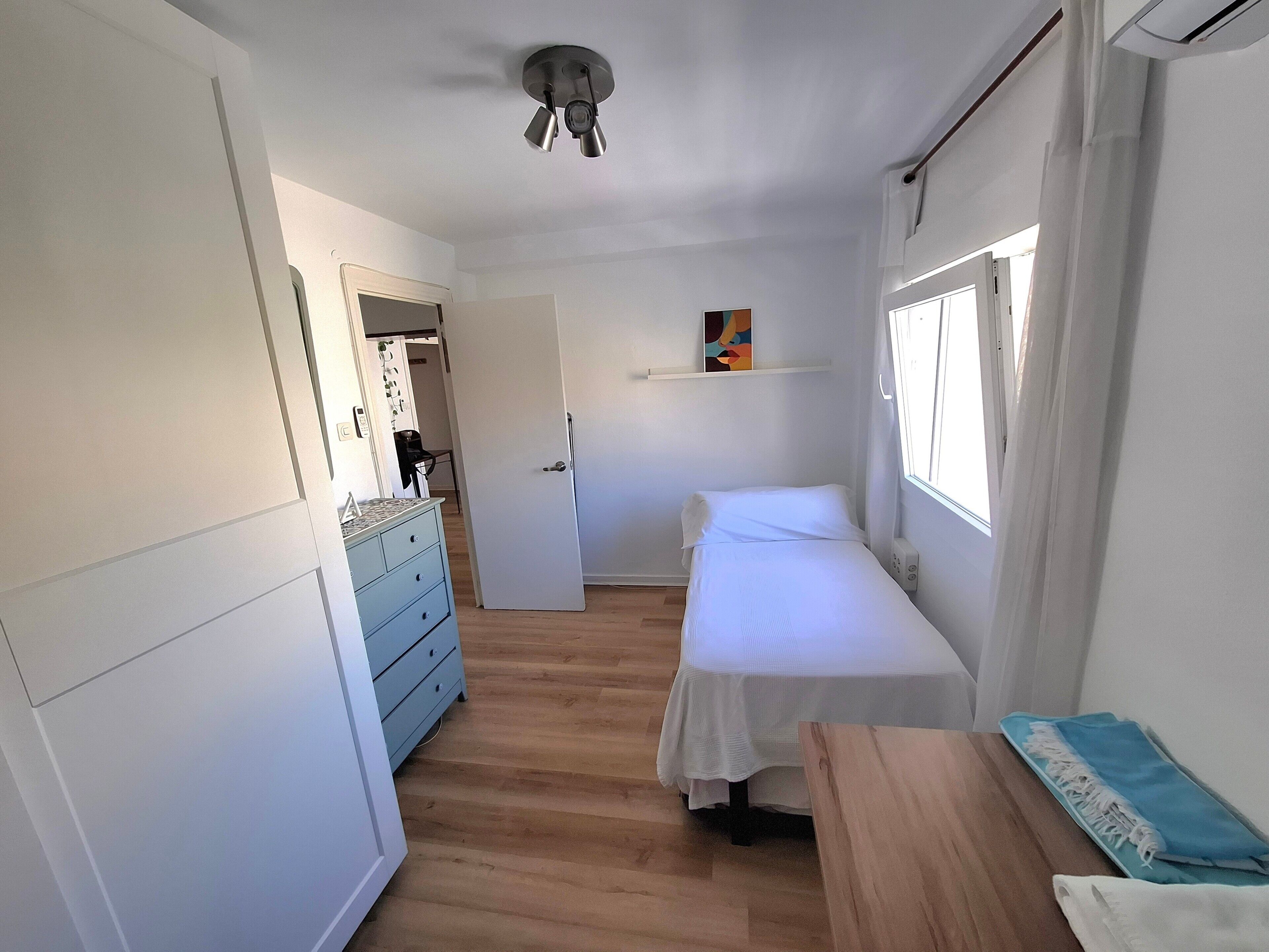 Un dormitorio con cama, cómoda, escritorio, ventana y lámpara en el techo.