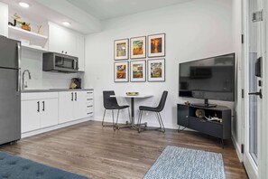 Een moderne keuken met witte kasten, een roestvrijstalen koelkast, een magnetron en een eethoek met een tafel en stoelen.