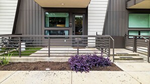 Un edificio moderno con tetto piatto, un balcone e un piccolo giardino con piante viola.